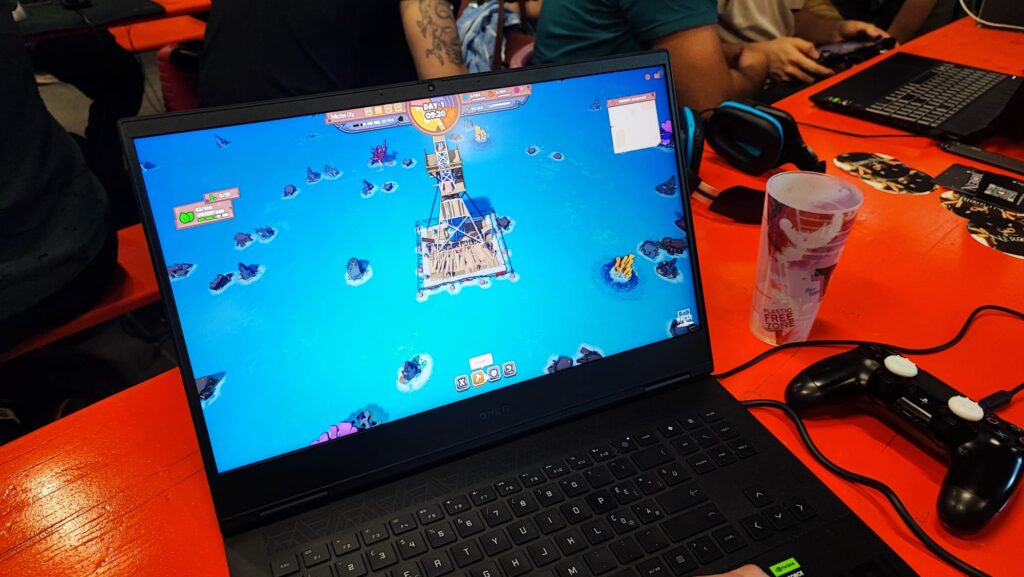 Laptop gaming su tavolo arancione durante un evento videoludico con videogioco strategico sullo schermo.