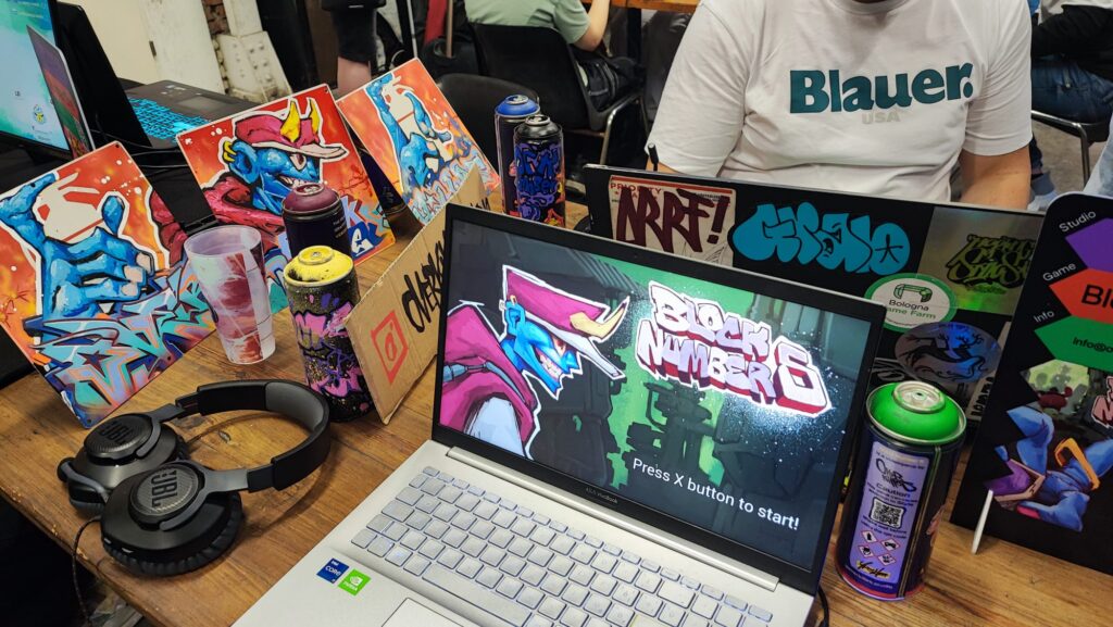 Postazione di gioco con laptop aperto su un videogioco a tema graffiti, bombolette spray e illustrazioni artistiche.